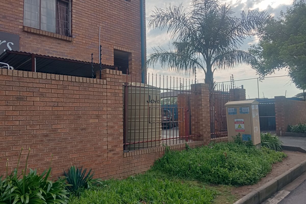 Exterior view of the apartment complex featuring face brick construction, perimeter security fencing, and a water storage tank.