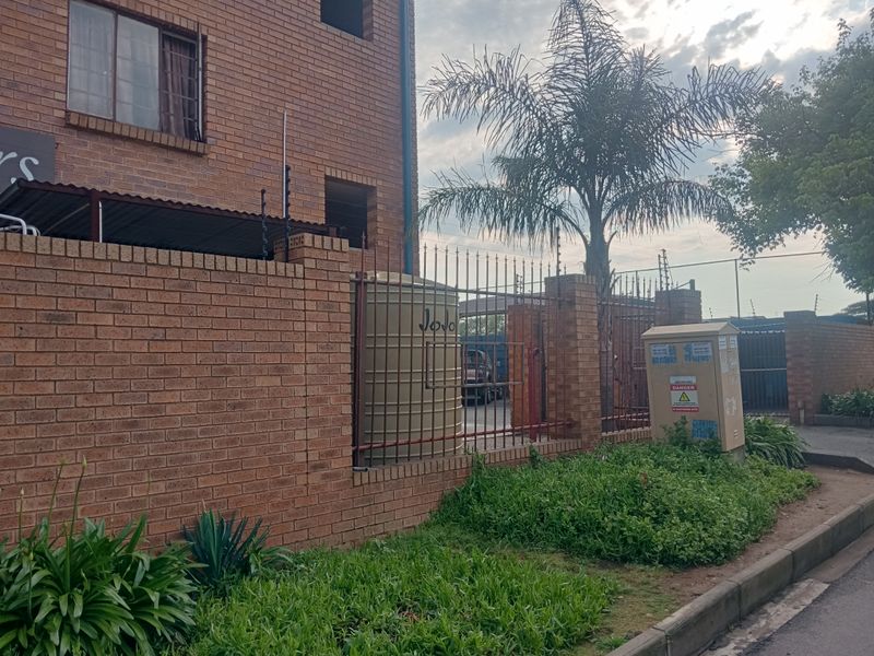 Exterior view of the apartment complex featuring face brick construction, perimeter security fencing, and a water storage tank.
