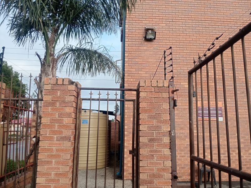 Rear exterior area featuring a brick perimeter wall, metal security gate with electric fencing, and a water storage tank.