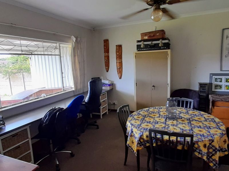 A living area featuring a ceiling fan, built-in storage cupboard, and a large window with security bars, offering a functional space with natural light.