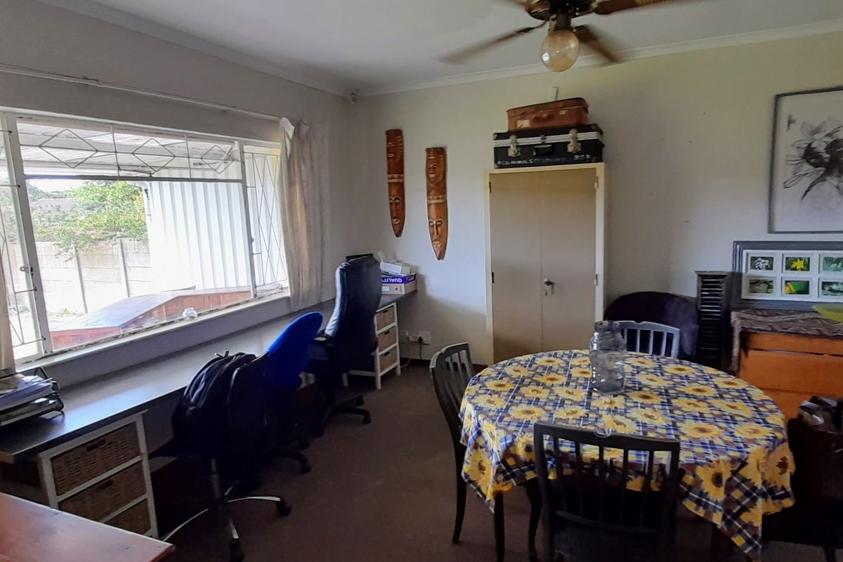 A living area featuring a ceiling fan, built-in storage cupboard, and a large window with security bars, offering a functional space with natural light.
