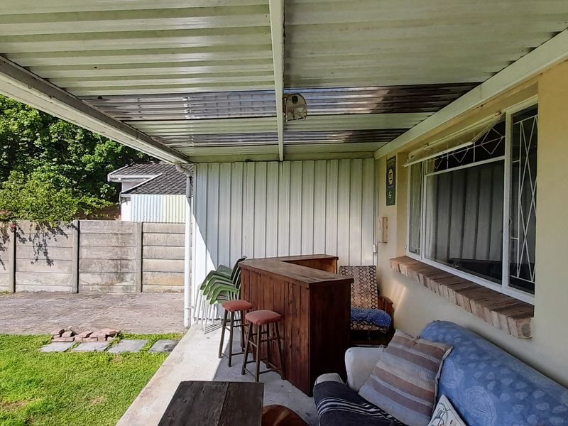 A covered outdoor patio area featuring a concrete floor, corrugated roof, and security-barred windows, providing a functional space for outdoor relaxation.
