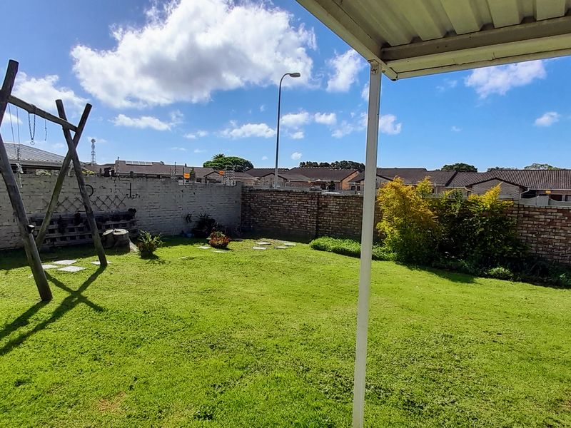 A rear garden featuring a lawn area, enclosed by brick boundary walls, viewed from a covered patio space.