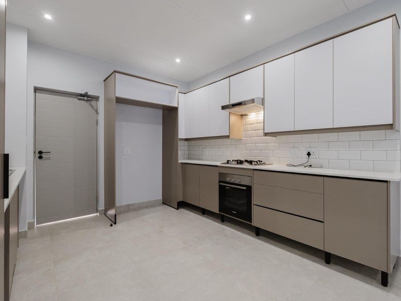 Modern kitchen featuring sleek two-tone cabinetry, subway tile backsplash, integrated gas hob, oven, and extractor fan with neutral tiled flooring.