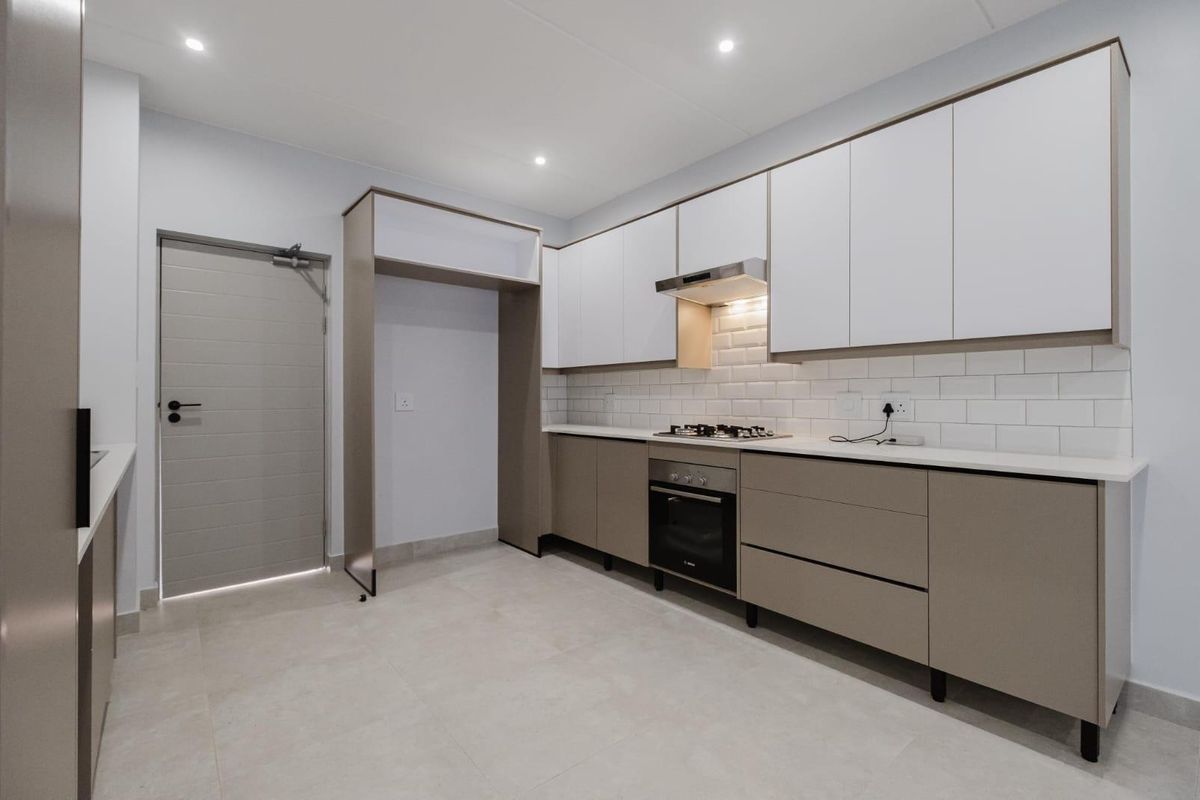 Modern kitchen featuring sleek two-tone cabinetry, subway tile backsplash, integrated gas hob, oven, and extractor fan with neutral tiled flooring.