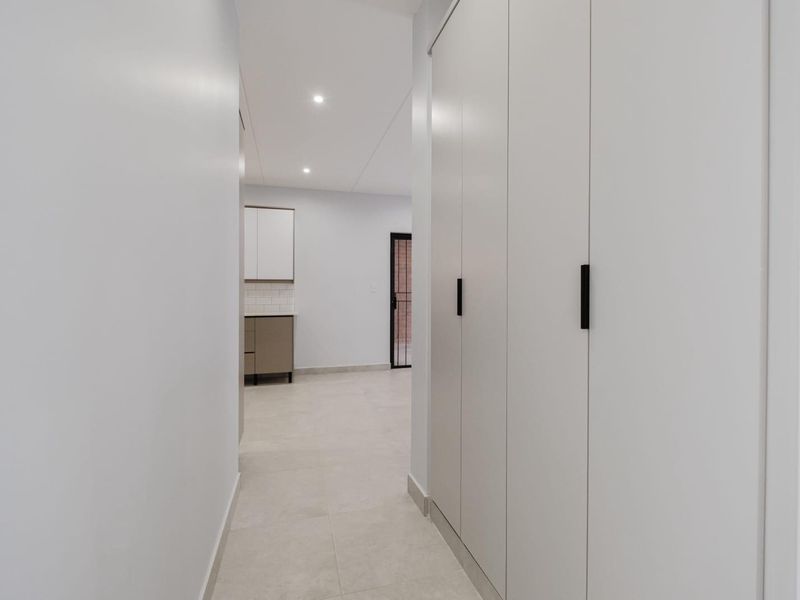 A clean, modern hallway featuring neutral tiled flooring, recessed downlighting, and extensive built-in storage cabinetry with sleek black handles.