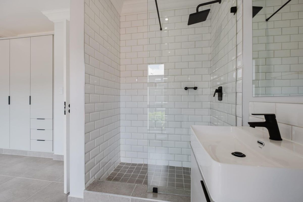 Modern bathroom featuring a walk-in shower with subway tiling, black matte fixtures, and a sleek vanity, adjacent to a built-in wardrobe.