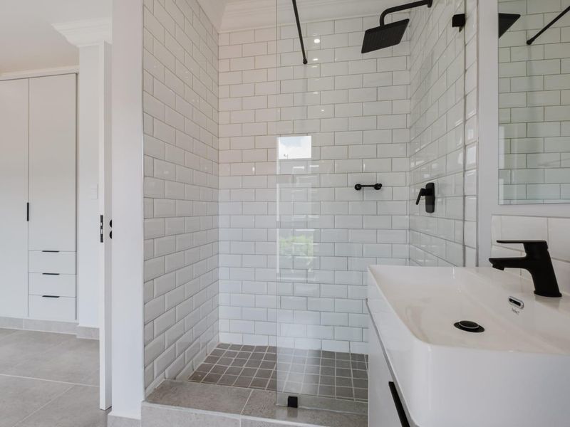 Modern bathroom featuring a walk-in shower with subway tiling, black matte fixtures, and a sleek vanity, adjacent to a built-in wardrobe.