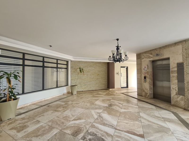 A spacious and well-maintained apartment building lobby featuring elegant stone tile flooring, a feature stone wall, and a modern elevator access point.