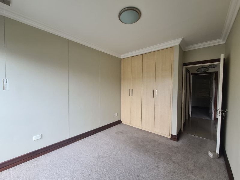 A clean, empty bedroom featuring neutral wall tones, carpeted flooring, and ample built-in cupboard storage space.