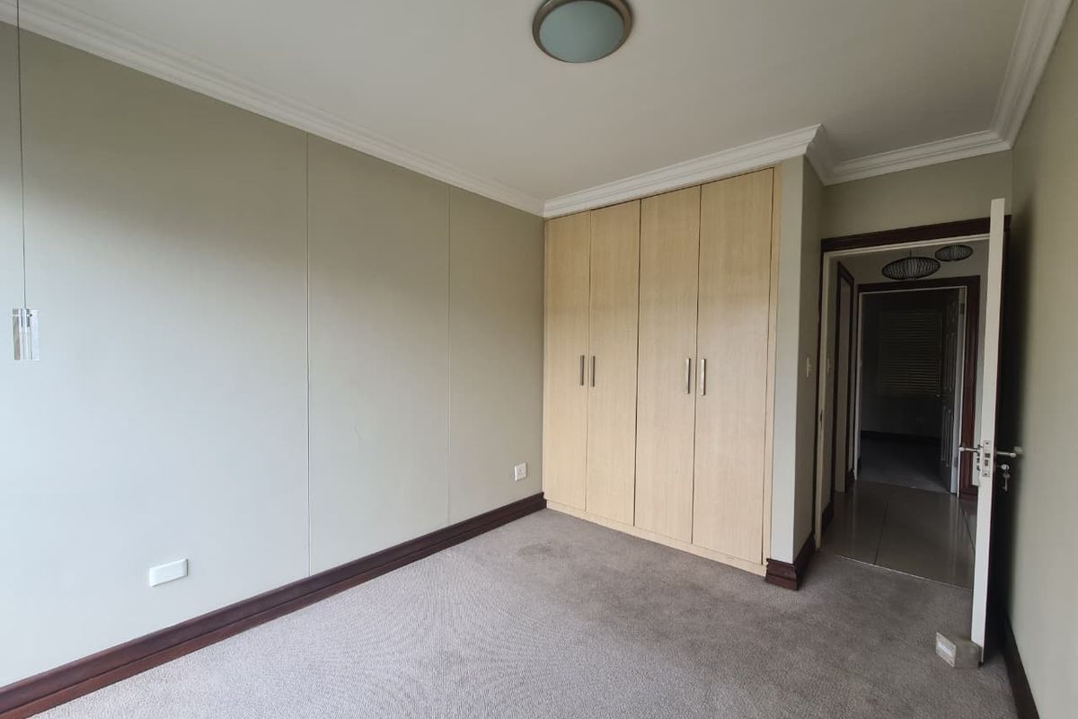 A clean, empty bedroom featuring neutral wall tones, carpeted flooring, and ample built-in cupboard storage space.
