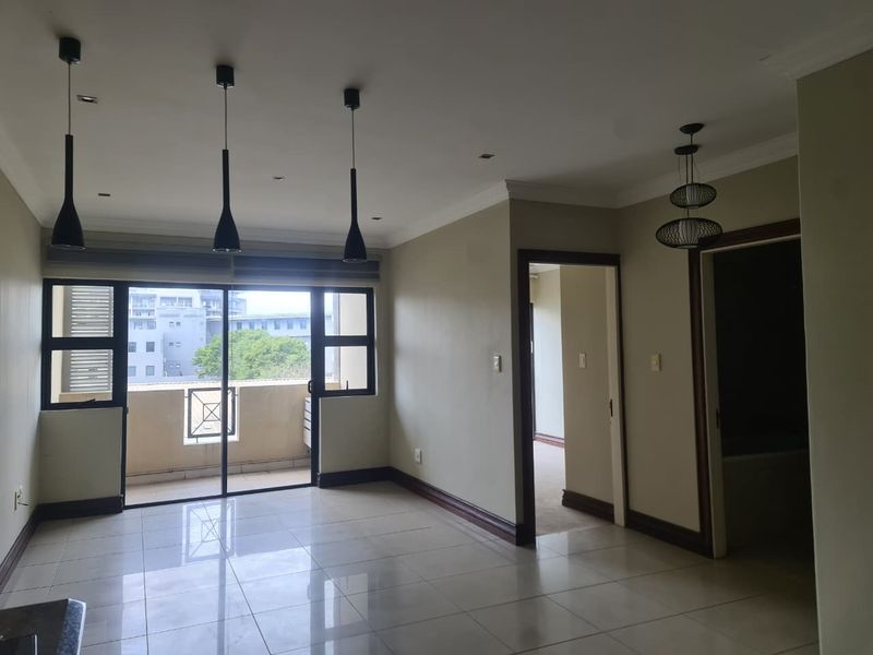 Spacious, light-filled living area featuring neutral tiled flooring, modern pendant lighting, and direct access to a private balcony through sliding glass doors.
