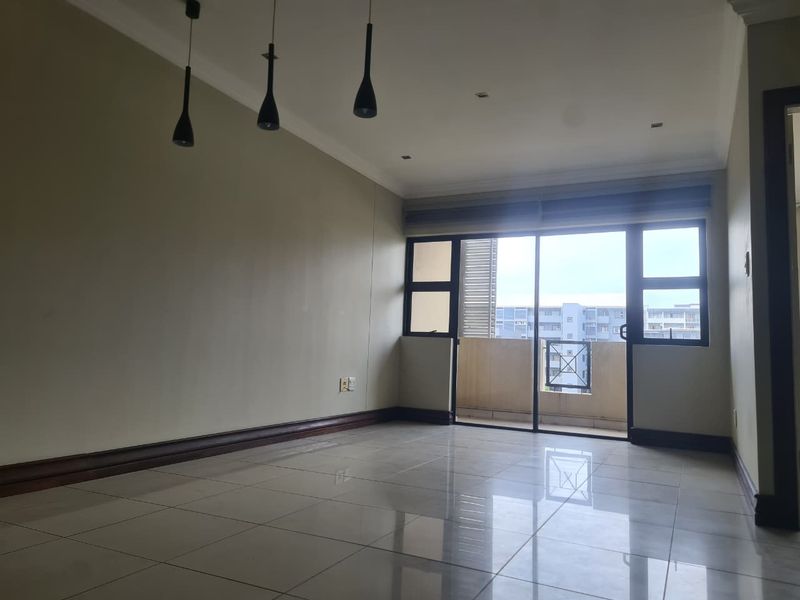 A bright and spacious empty living area featuring polished tile flooring, modern pendant lighting, and a sliding glass door leading to a private balcony.