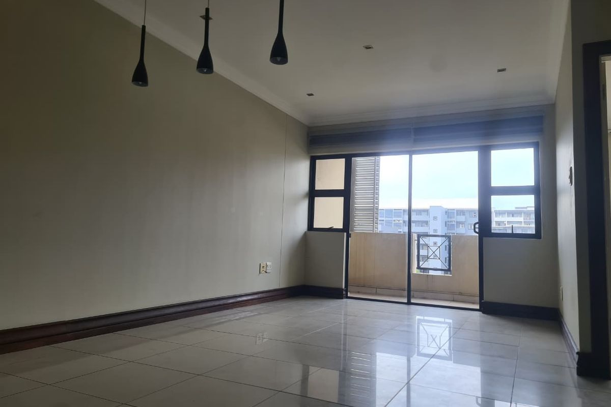 A bright and spacious empty living area featuring polished tile flooring, modern pendant lighting, and a sliding glass door leading to a private balcony.