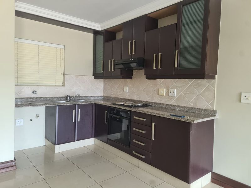 A functional kitchen featuring dark wood cabinetry, granite countertops, built-in oven, hob, and extractor fan, with a neutral tiled backsplash and flooring.