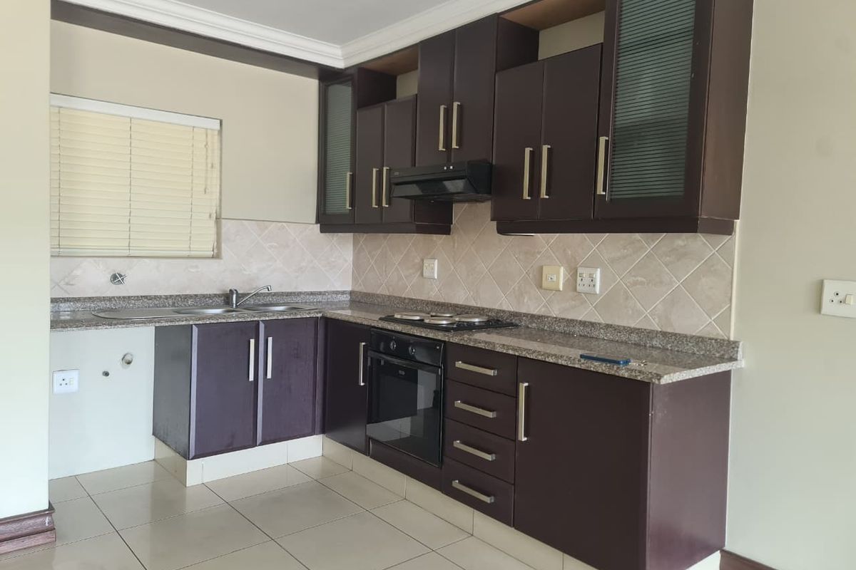 A functional kitchen featuring dark wood cabinetry, granite countertops, built-in oven, hob, and extractor fan, with a neutral tiled backsplash and flooring.