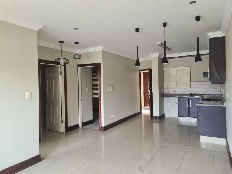 Spacious open-plan living area featuring tiled floors, neutral walls, and a functional kitchen with granite countertops and built-in cabinetry.