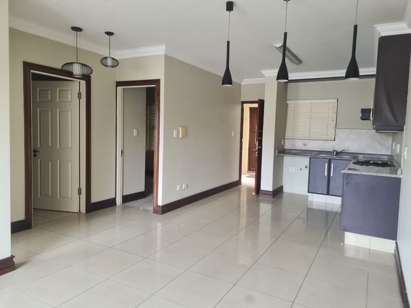 Spacious open-plan living area featuring tiled floors, neutral walls, and a modern kitchen with granite countertops and built-in cabinetry.