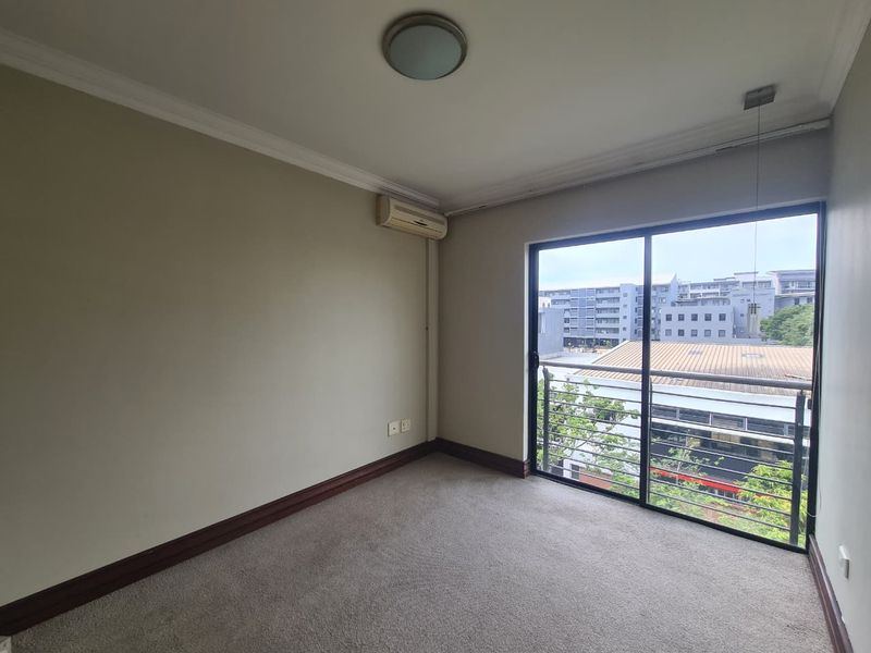 An empty bedroom featuring carpeted flooring, a wall-mounted air conditioning unit, and a sliding glass door leading to a balcony with neighborhood views.