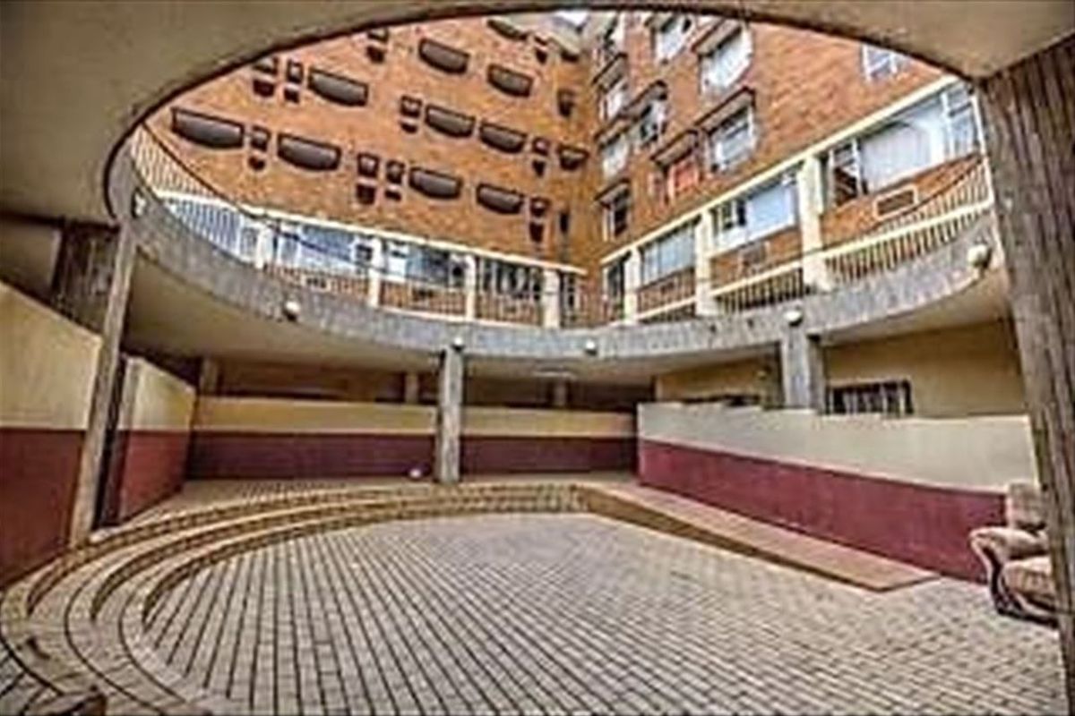 A view of the apartment complex's central paved courtyard, featuring a ramp, concrete columns, and multi-story brick facade with balcony railings.