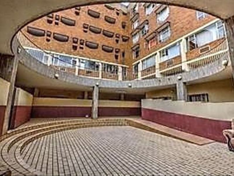 A view of the apartment complex's central paved courtyard, featuring a ramp, concrete columns, and multi-story brick facade with balcony railings.