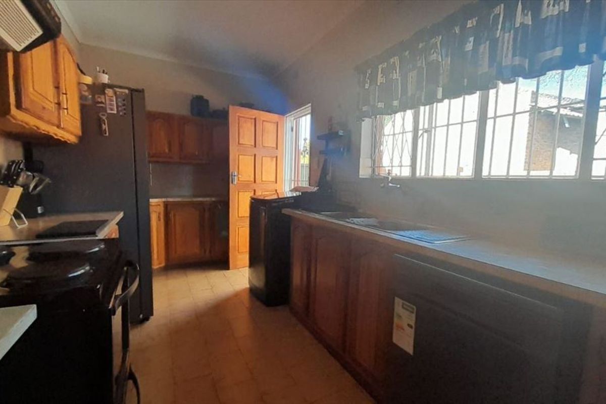 A functional kitchen featuring wooden cabinetry, laminate countertops, and a double basin sink, with security bars installed on the windows.