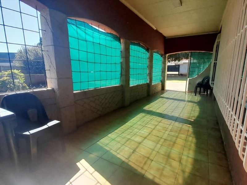 A covered patio area featuring tiled flooring, security bars, and arched masonry pillars, providing a functional outdoor space.