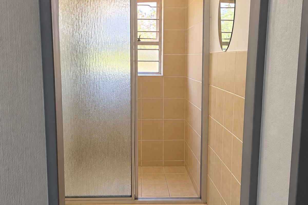 A clean, functional bathroom featuring a walk-in shower with a sliding glass door, neutral ceramic tiling, and a window for natural light.