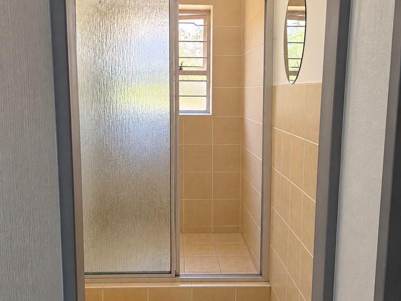 A clean, functional bathroom featuring a walk-in shower with a sliding glass door, neutral ceramic tiling, and a window for natural light.