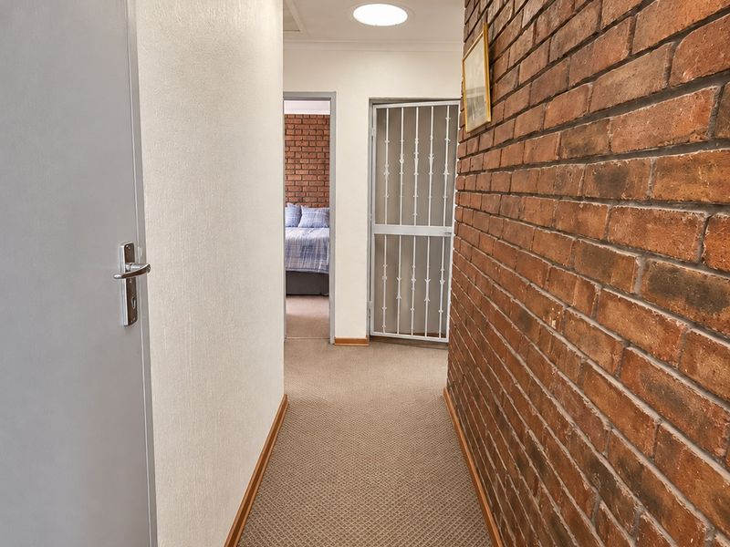 A well-lit hallway featuring a prominent exposed brick wall, neutral carpeting, and a security gate leading to an adjacent room.