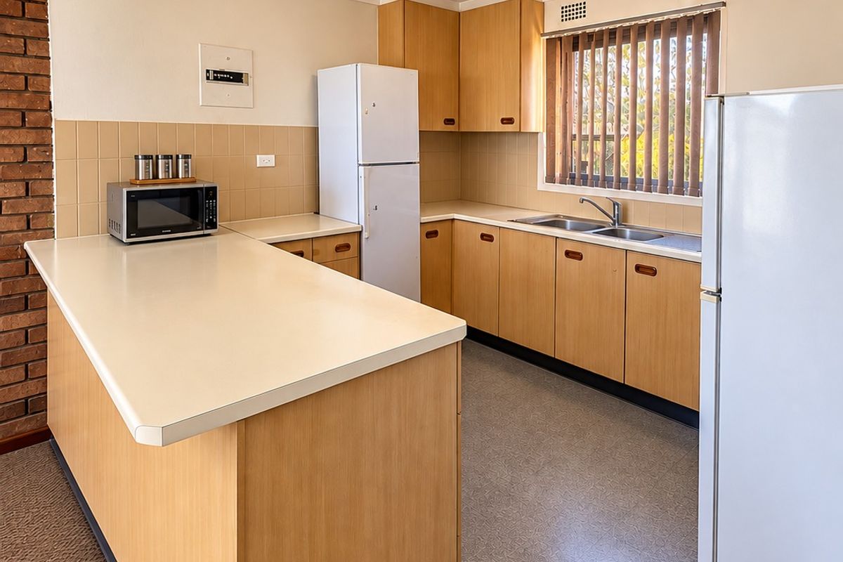 A functional kitchen featuring laminate cabinetry, a double bowl sink, tiled splashback, and a distinctive brick feature wall, offering a practical layout.