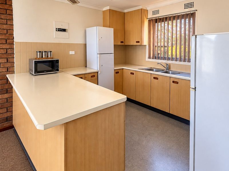 A functional kitchen featuring laminate cabinetry, a double bowl sink, tiled splashback, and a distinctive brick feature wall, offering a practical layout.
