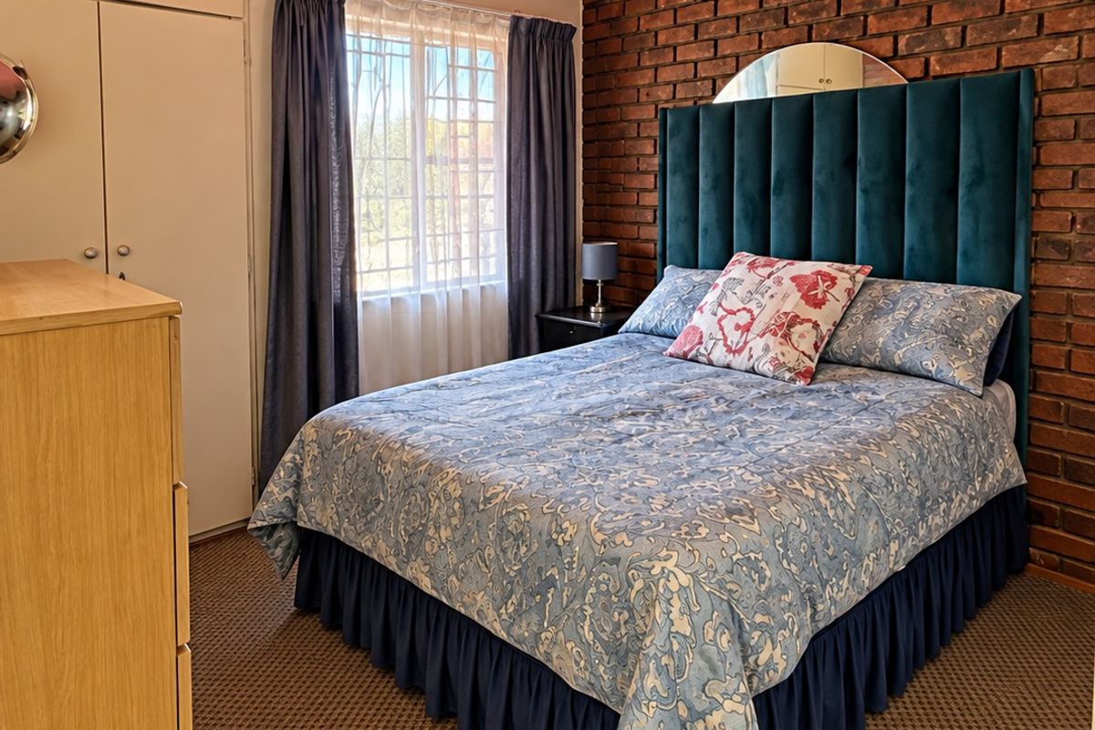A bedroom featuring an exposed brick wall, built-in cupboards, and carpeted flooring, offering a unique character with potential for modern updates.