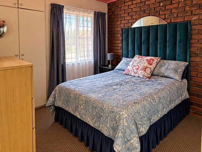 A bedroom featuring an exposed brick wall, built-in cupboards, and carpeted flooring, offering a unique character with potential for modern updates.