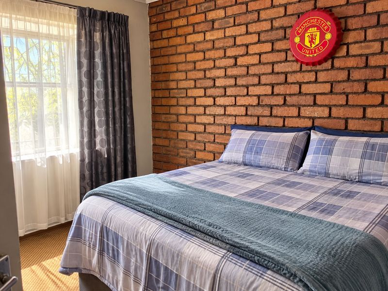 A bedroom featuring a prominent exposed brick feature wall and a window fitted with security bars.