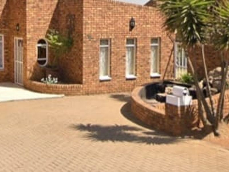 A well-maintained face brick exterior featuring a paved driveway, arched garage entrance, and landscaped retaining wall area.