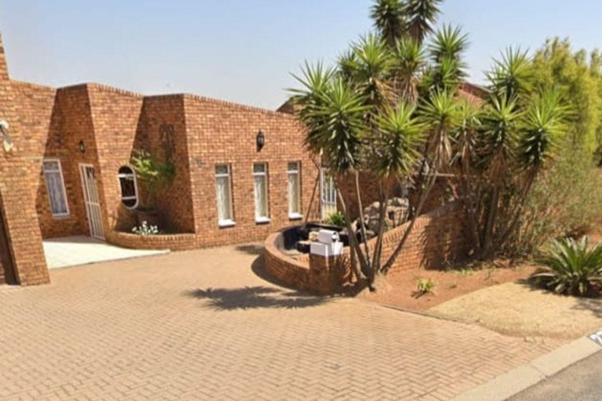 Front elevation of a face brick house featuring a paved driveway, established garden, and secure entrance.