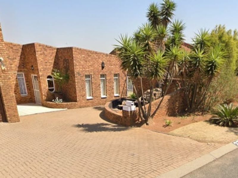 Front elevation of a face brick house featuring a paved driveway, established garden, and secure entrance.