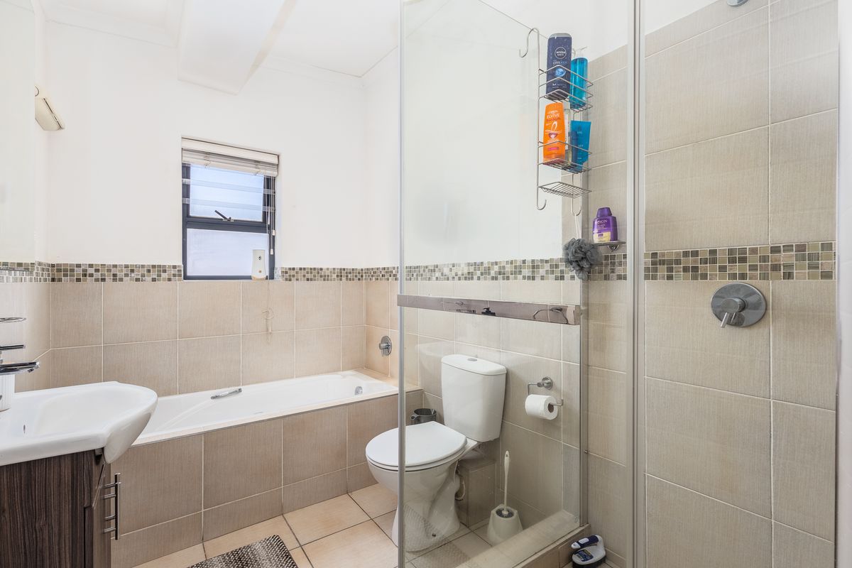 A well-maintained bathroom featuring a built-in bathtub, a separate glass-enclosed shower, neutral ceramic tiling, and a modern vanity basin.