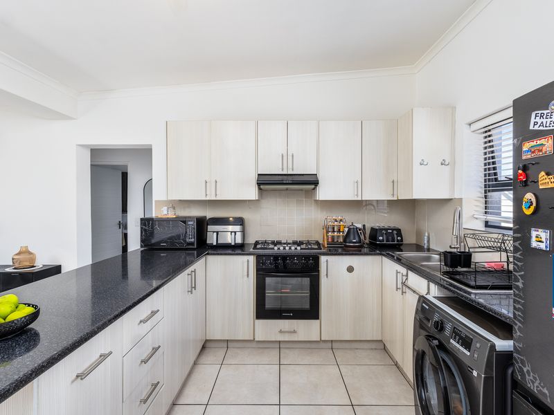 A functional kitchen featuring light wood-finish cabinetry, dark granite countertops, a gas hob with extractor, and tiled flooring.