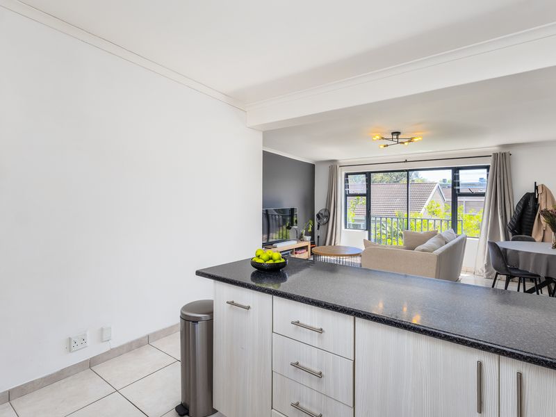 Open-plan living area featuring a modern kitchen with granite countertops, tiled flooring, and seamless flow to a balcony with natural light.