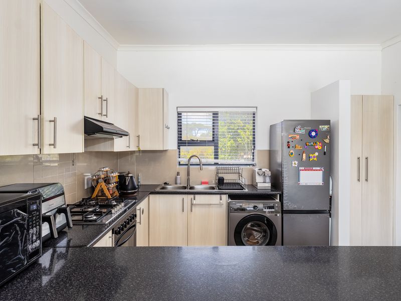 A functional kitchen featuring light wood-finish cabinetry, dark granite countertops, a gas hob with extractor fan, and a stainless steel sink.