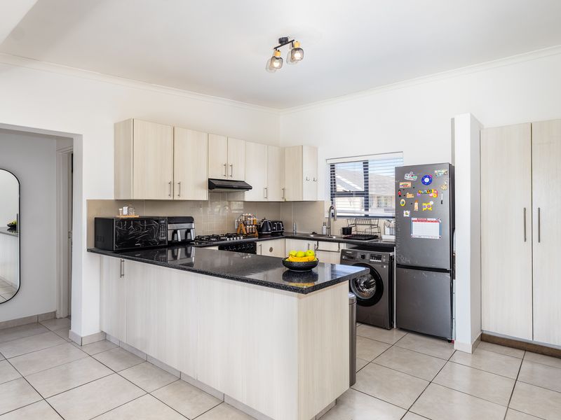 A functional kitchen featuring light wood cabinetry, granite countertops, a gas hob, and tiled flooring, with an adjacent pantry and open-plan layout.
