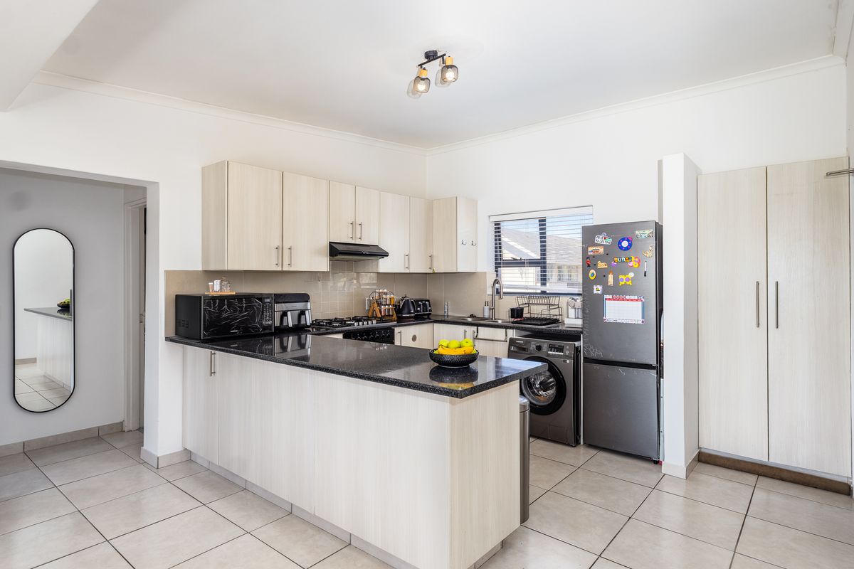 A functional kitchen featuring light wood cabinetry, granite countertops, a gas hob, and tiled flooring, with an adjacent pantry and open-plan layout.