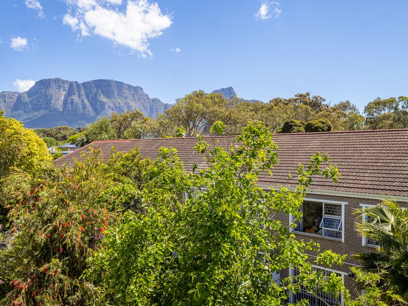 Elevated view overlooking a residential building with a tiled roof, surrounded by mature trees and featuring a scenic mountain backdrop.