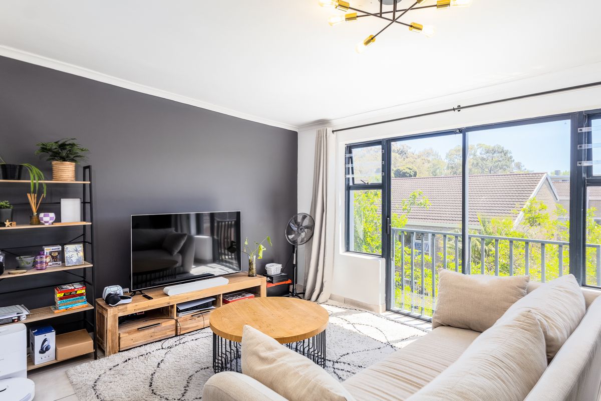 A bright and modern living room featuring a dark accent wall, large sliding glass doors leading to a balcony, and contemporary lighting.