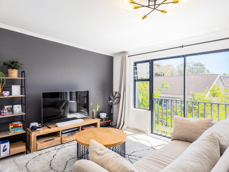 A bright and modern living room featuring a dark accent wall, large sliding glass doors leading to a balcony, and contemporary lighting.
