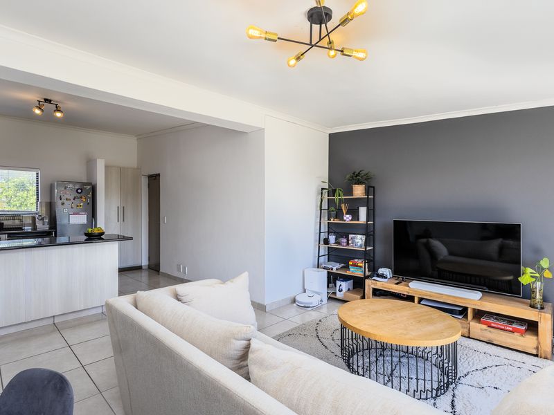 An open-plan living area featuring a modern kitchen with granite countertops, tiled flooring, and a stylish accent wall in the lounge space.