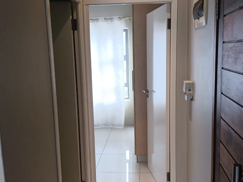 A clean, well-maintained hallway featuring neutral tiled flooring and access to adjacent rooms, providing a bright and functional transition space within the apartment.