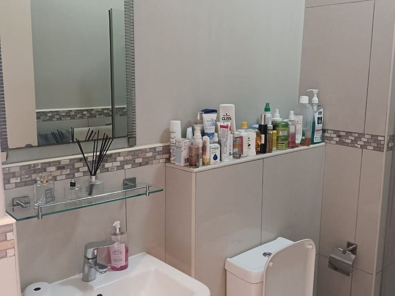 A functional bathroom featuring a pedestal basin, toilet, wall-mounted mirror, and decorative mosaic tile accents.